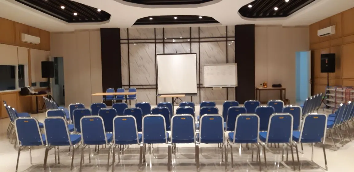 Aula dengan kursi biru tertata menghadap layar proyektor