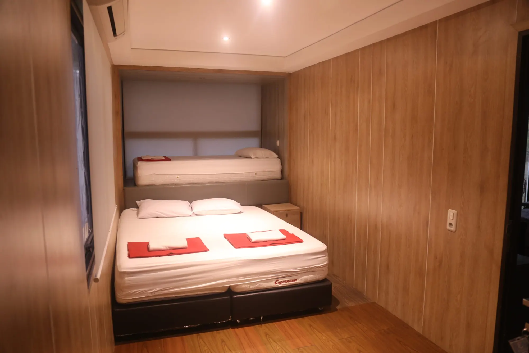 Kamar tidur rumah kontainer dengan dinding kayu dan handuk merah