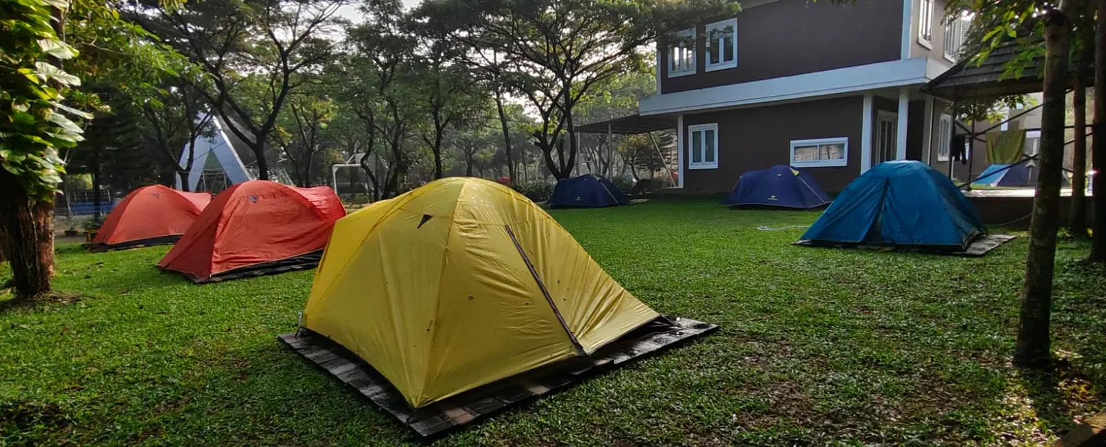 Tenda-tenda berwarna berdiri di halaman berumput di depan rumah penginapan
