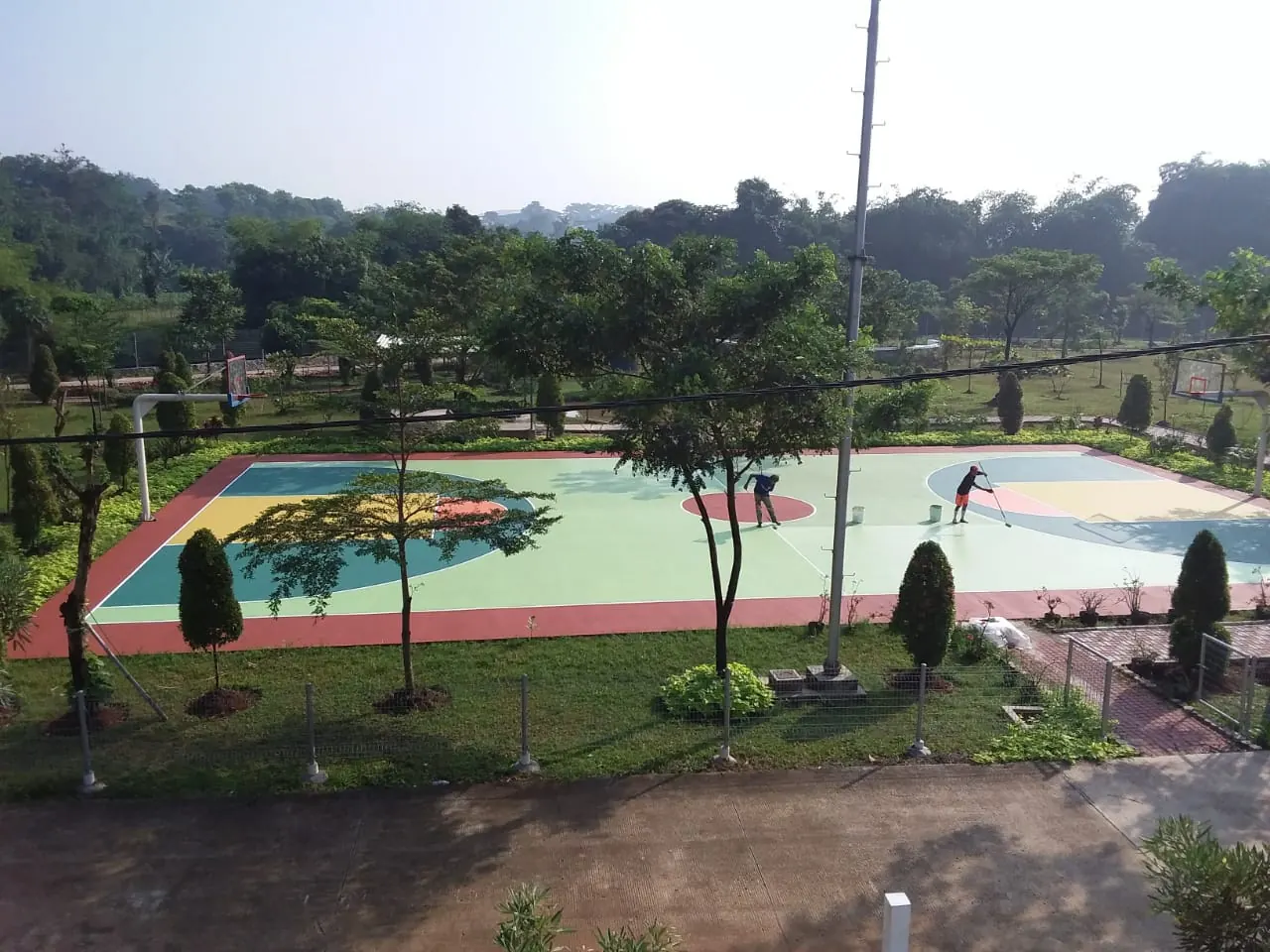 Lapangan basket hijau dilihat dari atas dengan perbukitan di latar