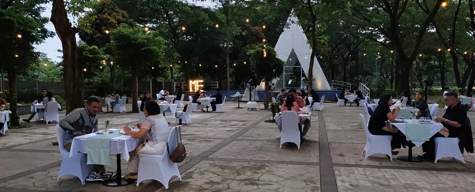 Tamu makan malam di meja bertaplak putih di pelataran, Chapel LWJ di latar