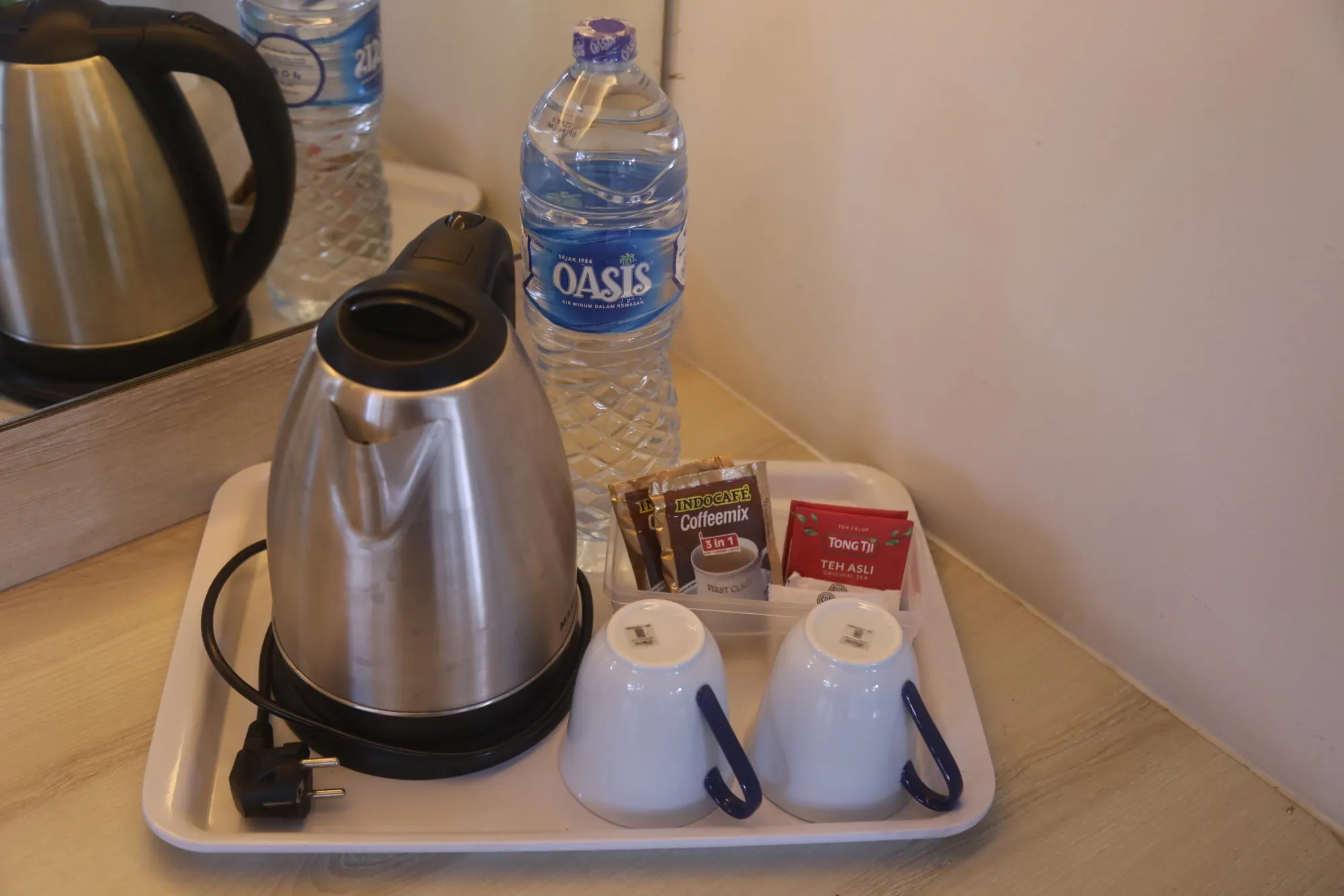 Nampan berisi teko listrik, cangkir, air mineral, dan sachet kopi